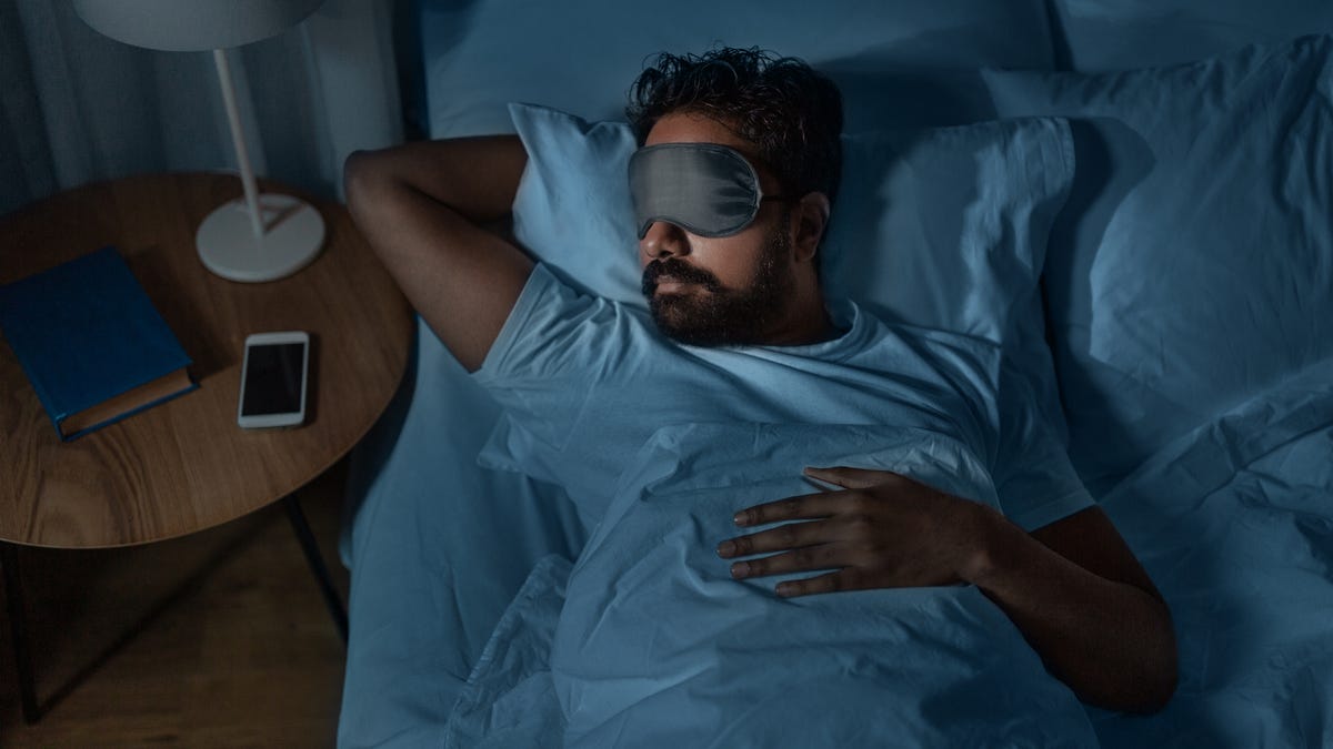 A man sleeping in bed with a mask over his eyes.
